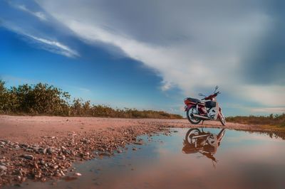 Motorcycle on dirt road against cloudy sky