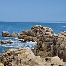 Scenic view of rocks by sea against clear sky