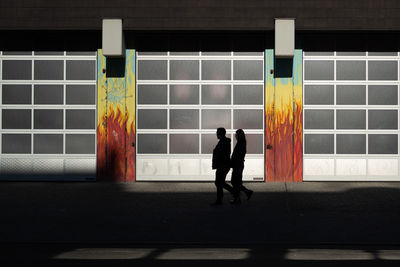 Rear view of man walking on footpath against building