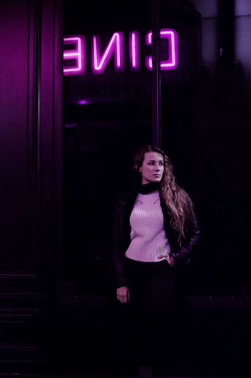 one person, front view, illuminated, real people, young adult, standing, long hair, lifestyles, night, indoors, young women, leisure activity, looking at camera, text, casual clothing, hairstyle, women, western script, dark, nightlife, teenager, contemplation, beautiful woman, purple