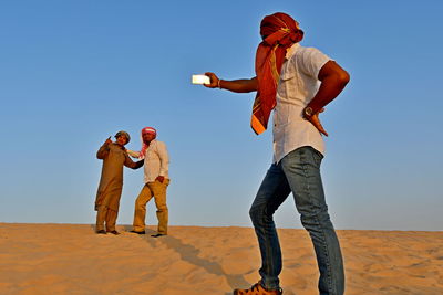 Man taking selfie while friends standing on desert against sky