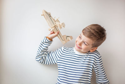 Smiling boy holding model airplane while sitting against white background