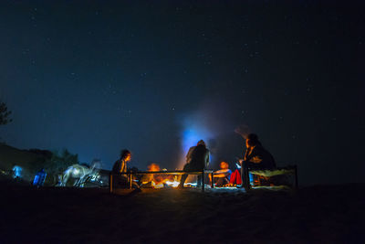 People sitting on land against sky at night