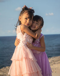 Side view of sisters standing at beach against sky