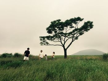 Family walking on grassy land against clear sky