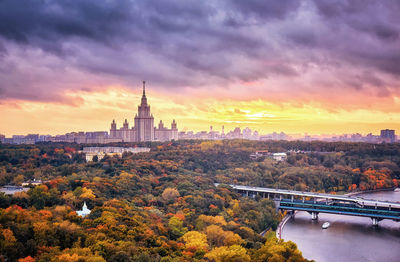 View of trees in city against cloudy sky during sunset