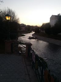 Footpath by river against buildings in city at dusk