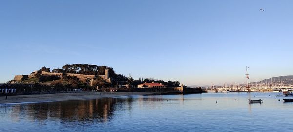 Scenic view of river by buildings against clear blue sky