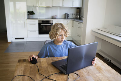 Boy studying through laptop on table at home