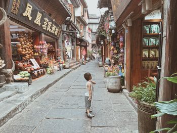 Rear view of boy walking on street amidst buildings