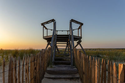 Metallic structure on footpath against sky during sunset