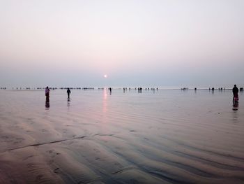 Group of people on beach against sky during sunset