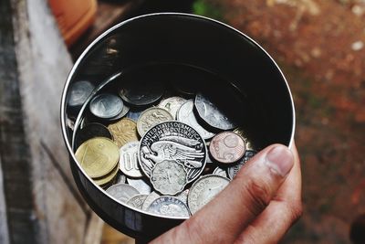 Close-up of hand holding coins in container