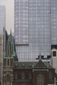 Old church with stone facade on background of contemporary tall skyscraper with glass mirrored walls in new york