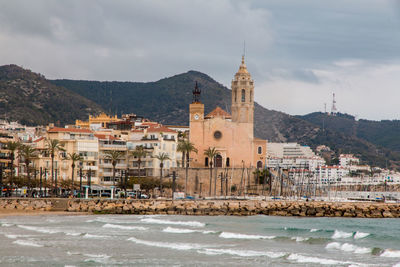 Buildings at waterfront against cloudy sky