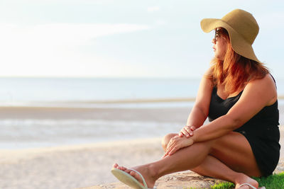 Woman wearing hat on beach against sky