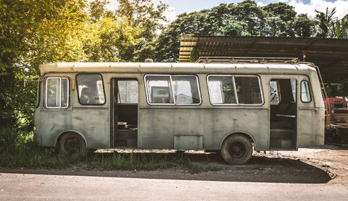 Abandoned vintage car parked on street against trees