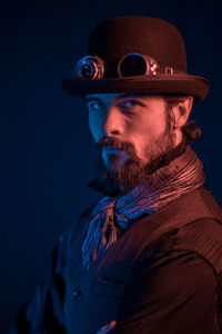 Portrait of man wearing hat and aviator glasses against black background