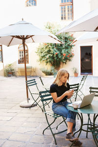 Young woman using mobile phone while sitting on chair at sidewalk cafe
