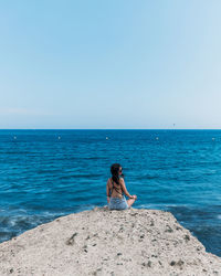 Full length of woman sitting on beach against clear sky