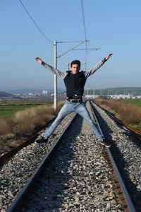 Full length of teenager jumping on railroad track against sky