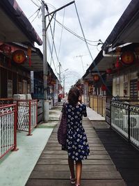 Rear view of woman walking on wooden road against sky