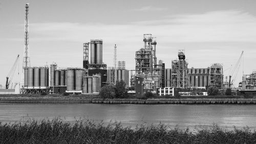 Factory by river against sky 