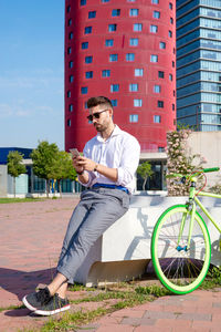 Outdoor portrait of handsome young man with mobile phone and fixed gear bicycle in the street.