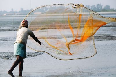 Rear view of man throwing fishing net at beach