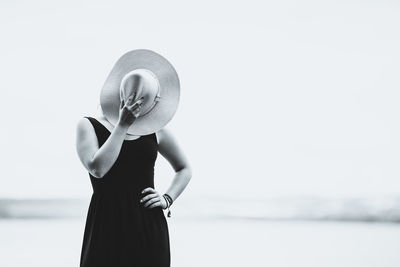 Woman covering face with hat while standing at beach against