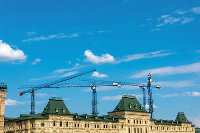 Low angle view of crane by building against blue sky