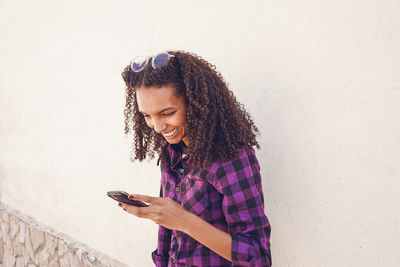 Young woman using mobile phone against wall