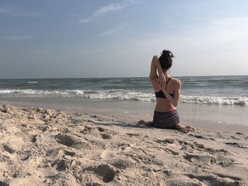 Rear view of young woman standing at beach against sky