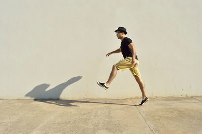 Full length of young man jumping on footpath against wall