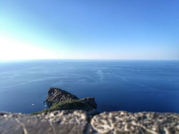 Close-up of rock by sea against clear blue sky