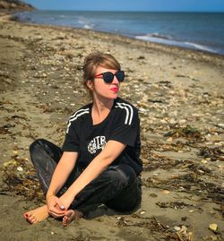 Young woman sitting on sunglasses at beach