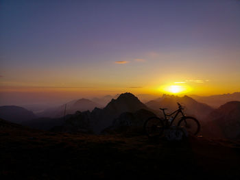 Silhouette bicycle against mountains during sunset