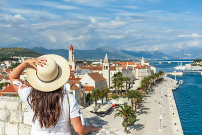 Rear view of woman standing on city walls looking at idyllic seaside town of trogir, croatia