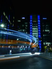 Light trails on street against illuminated buildings at night