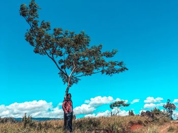 Person standing by tree on field against blue sky