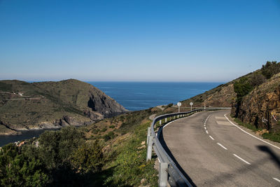 Scenic view of road by sea against clear blue sky
