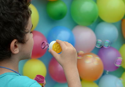 Cropped image of boy blowing bubbles against multi colored balloons