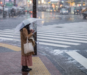 Woman with umbrella using mobile phone on sidewalk during winter
