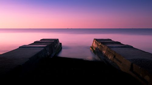 Wooden posts on beach against sky during sunset