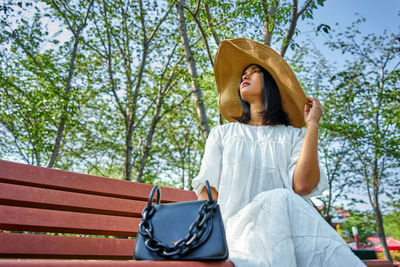 Young woman looking away while sitting on tree against plants