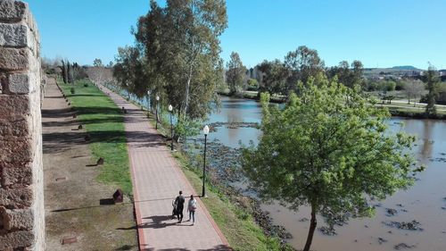 People walking on footpath by river against sky