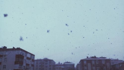 Low angle view of buildings seen through wet glass window