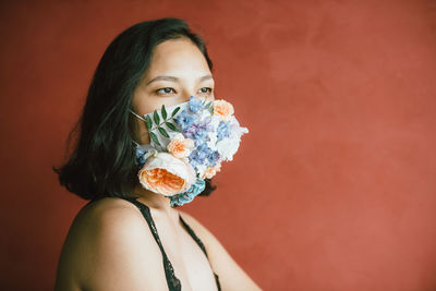 Close-up of woman wearing floral mask against red wall