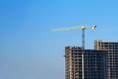 Low angle view of crane by building against clear blue sky