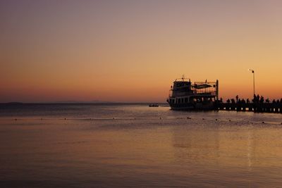 Silhouette ship and people on sea against sky during sunset